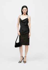 Zwarte satijnen cami met een gedrapeerde halslijn, gecombineerd met een bruine kokerrok met luipaardprint. Accessoires zijn een zwarte leren handtas en sandalen met bandjes.