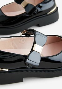 Zwarte gepatineerde leren schoenen met een dikke zool, voorzien van een strikaccent en gouden details. Het interieur is lichtroze met een gestructureerde afwerking.
