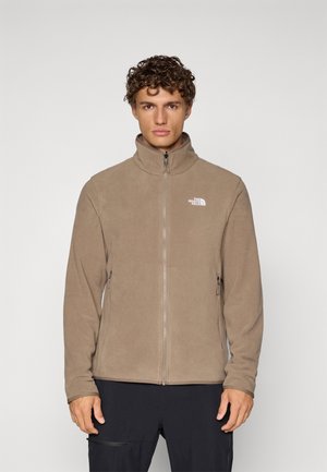 Chaqueta de forro polar beige con cuello alto, cierre de cremallera en la parte delantera y dos bolsillos laterales. Presenta un logo blanco en la parte superior izquierda. Textura suave.