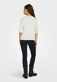 Biała, oversize koszulka z krótkim rękawem, zestawiona z ciemnymi denimowymi slim fit jeansami. Czarne kozaki za kolano z widocznymi srebrnymi akcentami.