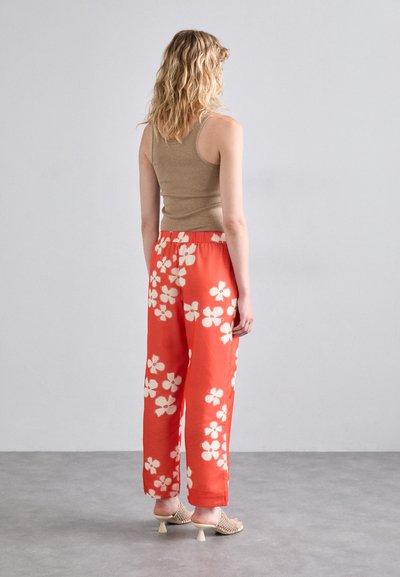 Beige tank top paired with bright red loose trousers featuring large white floral patterns. Visible back design and elastic waistband.