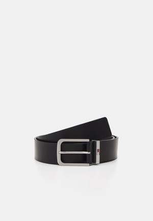 Cinturón de cuero negro con una hebilla de metal plateado de forma rectangular y un pequeño detalle de logo en la hebilla. Textura suave.
