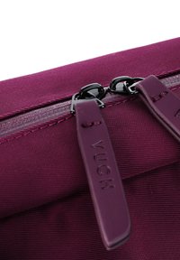 Bordeauxfarbene Reißverschlusstasche mit strukturiertem Stoffoberfläche. Verfügt über zwei schwarze Reißverschlusszieher mit geprägtem Branding auf den Riemen.