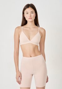 Bralette seamless rose clair avec des bretelles ajustables et un design en V, associé à un short de vélo taille haute à finition lisse.