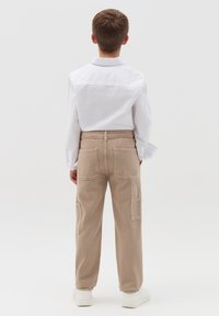 Beige cargobroek met meerdere zakken, van een katoenmix, rechte snit, gecombineerd met een wit overhemd met lange mouwen en kraag.