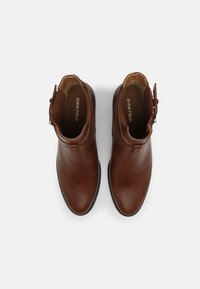 Ruskeat nahkaiset nilkkurit, joissa on sileä pinta, pyöreät kärjet ja sivulla säädettävä solki. Mukana joustava paneeli helppoa käyttöä varten.