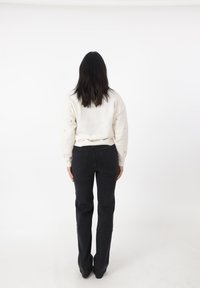 Maglione bianco oversize con dettagli testurizzati e polsini a coste, abbinato a jeans fitted neri a vita alta; visto da dietro.
