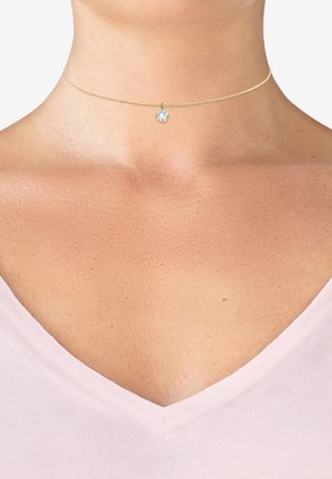 Goldene Choker-Halskette mit einer zarten Kette, die einen runden, klaren Edelstein-Anhänger in der Mitte trägt und über einem tiefen Ausschnitt ruht.