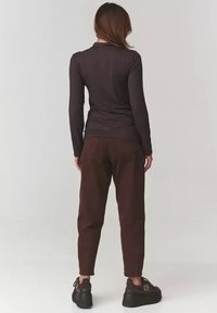 Długi rękaw, ciemno brązowa bluzka połączona z brązowymi spodniami, o luźnym kroju i teksturowanej tkaninie; czarne buty na platformie dopełniają stylizację.