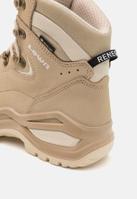 Beżowe buty trekkingowe z zamszowego materiału, wzmocnione szwy, metalowe oczka i teksturowana podeszwa. Posiadają czarną metkę z napisem "RENEGADE."