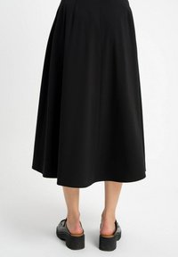 Czarna midi spódnica o zwiewnym kroju, wykonana z gładkiego materiału, z wysokim stanem i długością do połowy łydki.