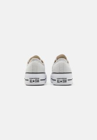 Weiße Leinenschuhe mit niedrigem Schnitt, schwarzen Akzenten, Gummisohle und "Converse All-Star"-Markierung an der Ferse.