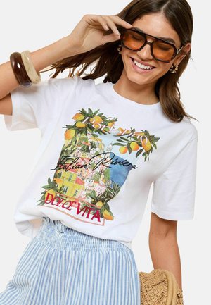 T-shirt en coton blanc avec un design graphique coloré d'une scène côtière, avec des oranges et un texte indiquant "Italian Riviera Dolce Vita."