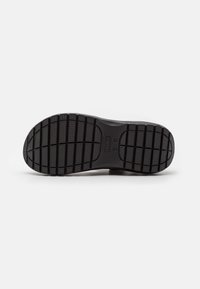 Suela de zapato Crocs negra con patrones de tread rectangulares y marcas de talla sobre un fondo blanco.