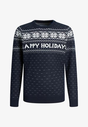 Granatowy sweter z napisem "WESOŁYCH ŚWIĄT", białe wzory płatków śniegu, ściągacze przy mankietach i dolnej krawędzi. Połączony z ciemnymi dżinsami i białymi sneakersami.