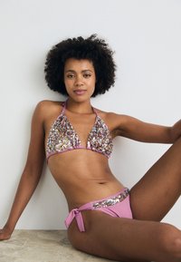 Pynk glitrande bikini sett, med halterneck topp med trekantede kopper og matchende lavt liv bukser med sidetopper. Glitrende detaljer hele veien.