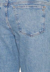 Calças de ganga azul claro com um bolso traseiro, apresentando um padrão de costura clássico e um tecido texturizado. Sem hardware ou adornos visíveis.