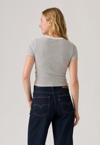 Striped short-sleeve t-shirt in grey and white, fitted design. Worn with dark blue denim jeans featuring a classic back pocket design.