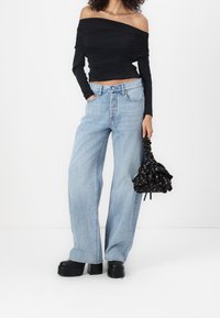 Black off-shoulder top, light blue high-waisted wide-leg jeans, black platform shoes, and a black floral drawstring bag.