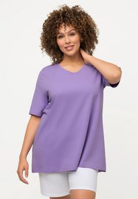 T-shirt a maniche corte e scollo a V, realizzata in tessuto morbido di colore viola chiaro. Indossata con pantaloni corti bianchi, caratterizzati da una vestibilità rilassata e dettagli con spacco laterale.