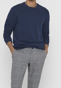 Sudadera de cuello redondo azul marino con mangas largas, combinada con pantalones de cuadros grises con líneas blancas y negras. Tejido de mezcla de algodón.