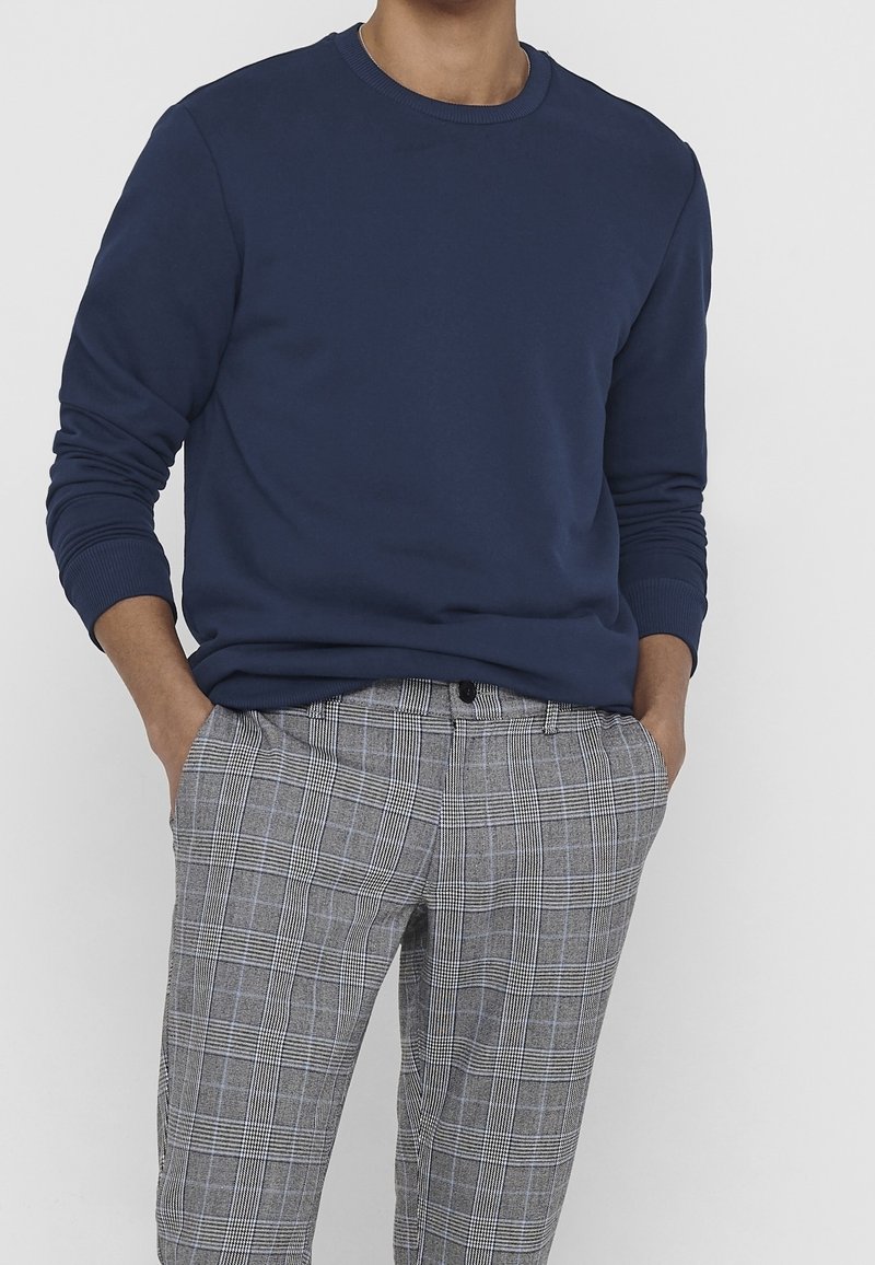 Sudadera de cuello redondo azul marino con mangas largas, combinada con pantalones de cuadros grises con líneas blancas y negras. Tejido de mezcla de algodón.