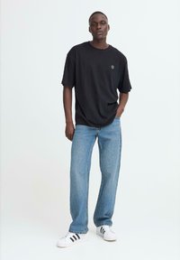 Svart oversized t-shirt, löst sittande ljusblå jeans och vita sneakers med svarta ränder. Enkel design, mjuk textur, avslappnad stil.