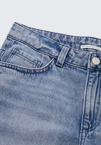 Světle modré džíny z denimu s vysokým pasem, viditelným švem, přední kapsou a štítkem s nápisem "vyrobeno z recyklovaných materiálů."