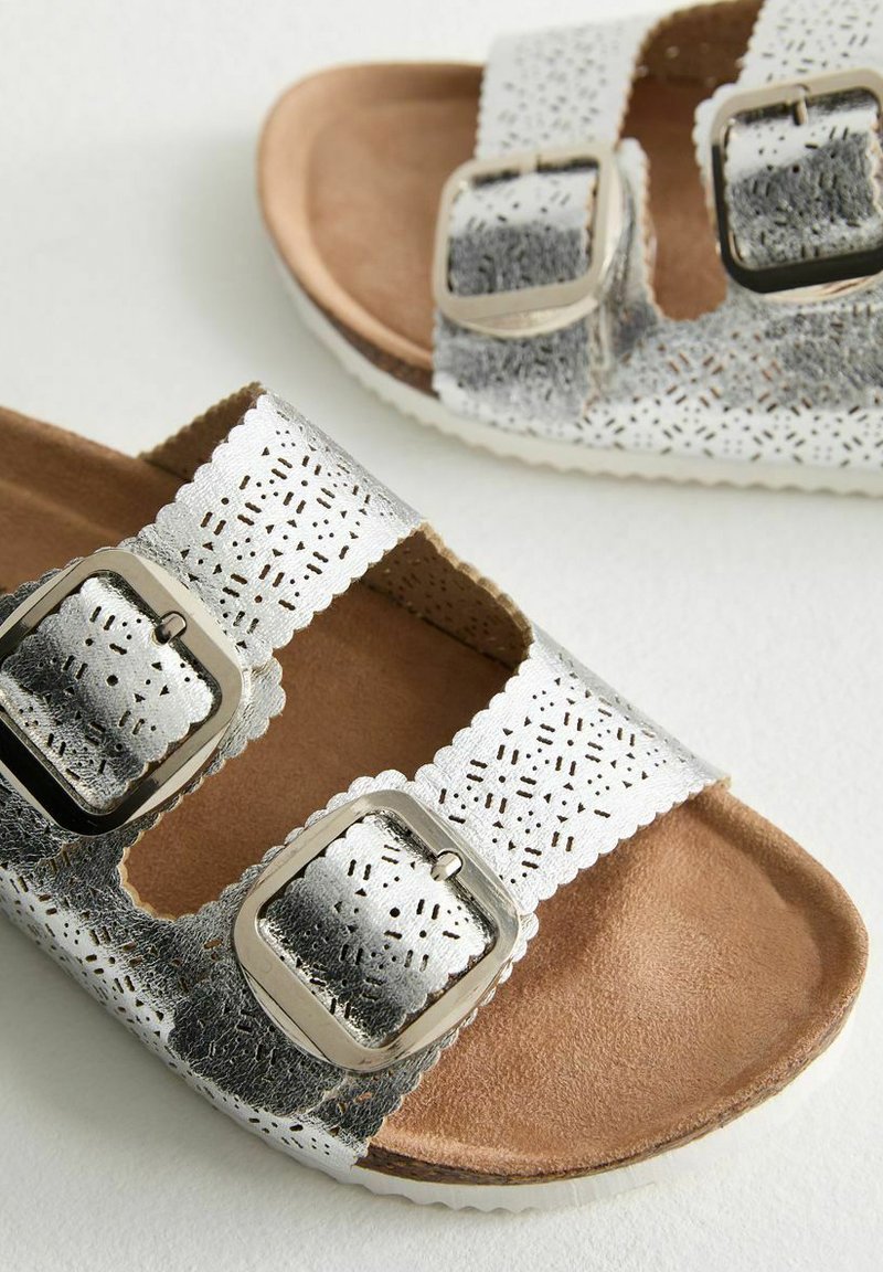 Złote sandały z ekipage z metalicznym srebrnym wykończeniem, perforowanym wzorem na paskach, brązowymi wkładkami z zamszu oraz teksturowanymi gumowymi podeszwami.