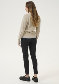 Beige ribbed sweater with a V-neck, featuring a textured pattern. Paired with black skinny jeans and platform loafers.