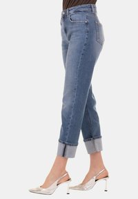 Jeans in denim azzurro chiaro con vita alta, gambe svasate e risvolti. Indossati con scarpe col tacco alto argentate per un look raffinato.