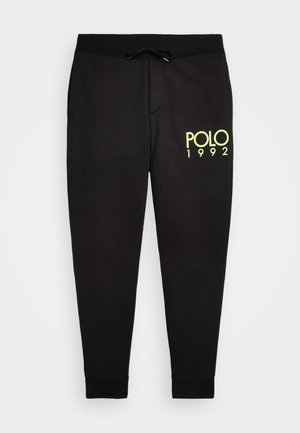 Pantaloni della tuta in cotone nero con vita elasticizzata e coulisse. Presentano una grafica gialla "POLO 1992" sulla gamba sinistra. Polsini aderenti.