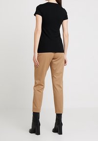 Sort kortærmet t-shirt kombineret med beige skræddersyede bukser og sorte hæle støvler. Glat stof med en tætsiddende silhuet og minimalistisk design.