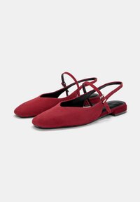 Rote Wildleder-Slingbacks mit spitzem Zehenbereich, Ausschnittdetails und einem dünnen Riemen mit einer silbernen Schnalle. Flache schwarze Sohle mit minimaler Textur.