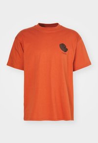 Camiseta de manga corta naranja con un gráfico de dispensador de cinta negra y pequeño texto en el lado izquierdo del pecho, sobre un fondo blanco.