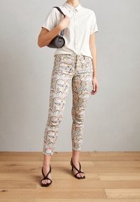 Světle béžová košile s knoflíky, vzorované pastelové jeansy s motivem paisley a černé sandály na podpatku. Malá černá kabelka s texturovaným povrchem.