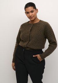 Brun stickad cardigan med ett strukturerat diamantmönster, rund halsringning och knappknäppning. Matcher med svarta byxor.
