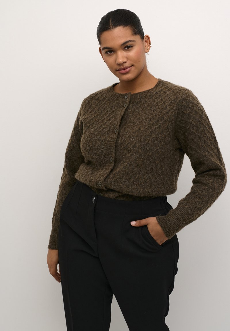 Brun stickad cardigan med ett strukturerat diamantmönster, rund halsringning och knappknäppning. Matcher med svarta byxor.