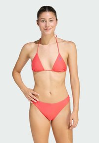 Koralowy bikini z trójkątnym stanikiem i szerokim dołem, wykonane z gładkiego materiału. Posiada cienkie ramiączka oraz małe niebieskie logo na staniku.