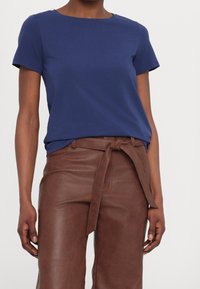 Camiseta de manga corta azul marino hecha de tejido suave, combinada con pantalones de cuero marrón de cintura alta con un detalle de cinturón atado.