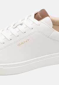 White leather sneaker with tonal stitching and round toe. Features white laces and a tan leather accent with gold "GANT" logo on the tongue.