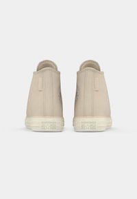 Baskets montantes beiges avec une texture en cuir lisse, semelles en caoutchouc et un petit logo sur le talon. Détails de couture subtils.