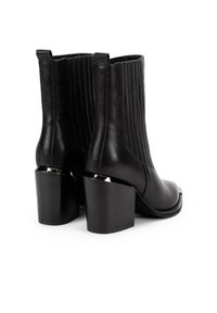 Pari mustista nahkasaappaista, joissa on paksut korot ja pystysuoraa ommelta sivuilla, esitelty takaa ja kyljeltä.