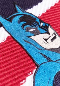 Geborduurde patch met een blauwe Batman-figuur op een gestructureerde rode en witte achtergrond met gedetailleerde stiksels en duidelijke gelaatskenmerken.