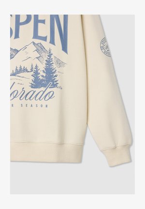 Beżowy sweatshirt z napisem "ASPEN" w niebieskim kolorze, grafiką gór, zielonymi drzewami iglastymi oraz prążkowanymi mankietami i dołem.