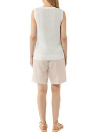 Leichtes, ärmelloses Stricktop in Weiß mit strukturiertem Muster, kombiniert mit hellrosa Shorts. Die Sandalen haben dünne Riemen.