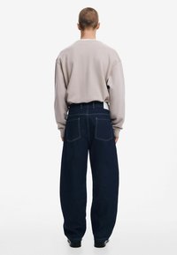Light gray oversized sweatshirt paired with dark blue wide-leg denim jeans. Features include large rear pockets and a clean waistband design.