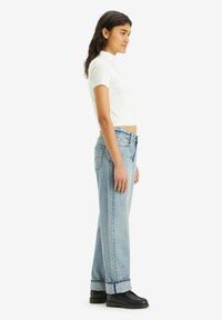 Afgekropte witte T-shirt, lichtblauwe high-waisted spijkerbroek met een wide-leg pasvorm, afgewerkt met een omgeslagen zoom, gecombineerd met zwarte enkelboots.