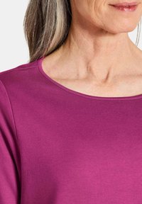 Fuchsia-Oberteil mit weicher Textur und rundem Ausschnitt, ausgestattet mit glatten Nähten und einem lockeren Schnitt.