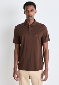 Brun polo skjorte laget av bomull, med en tre-knaps placket, korte ermer, og en liten logo på venstre bryst.